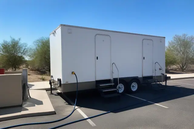 Luxury restroom trailer parked on asphalt in Surprise, AZ, with connected power cable and water hose.
