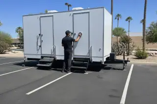 Technician cleaning the handle of a luxury restroom trailer on an asphalt parking lot in Phoenix, AZ.