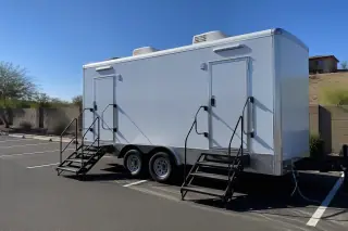 Luxury restroom trailer with water hoses parked on an asphalt lot in Phoenix, AZ.
