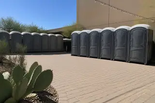 Portable toilets arranged on a paver patio with prickly pear cactus at an outdoor venue in Phoenix, AZ.
