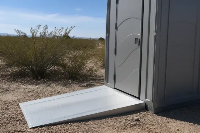 ADA-compliant portable toilet with a metal ramp on desert gravel in Phoenix, AZ.