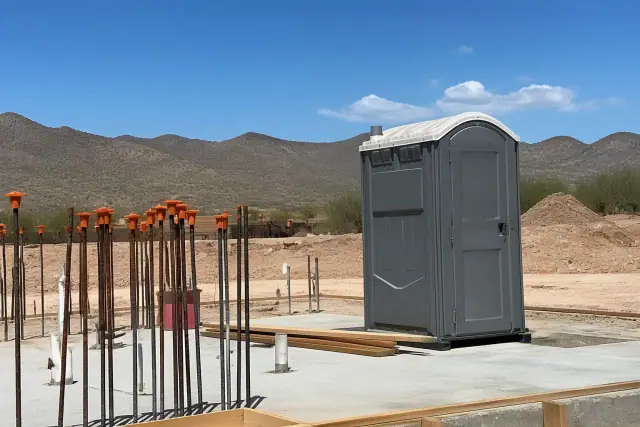 Standard portable toilets on a concrete jobsite foundation with desert mountains in the background in Phoenix, AZ.