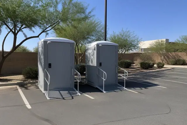 Wheelchair-accessible portable toilets on an asphalt parking lot in Phoenix, AZ, under bright desert sunlight.