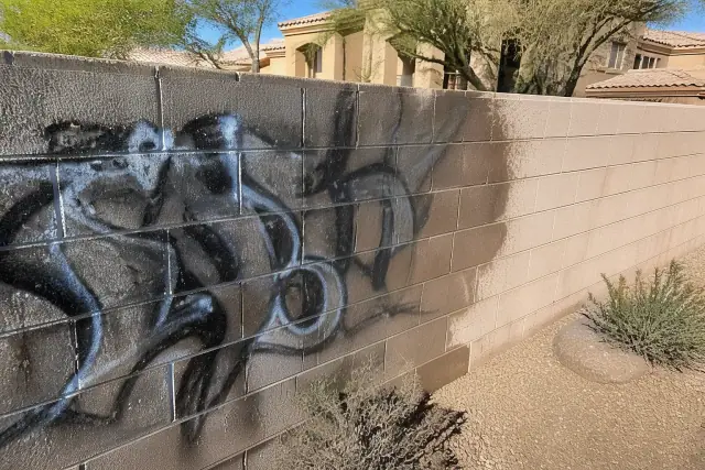 A clean masonry wall showing the transition from graffiti to original stone in a Phoenix, AZ desert landscape.