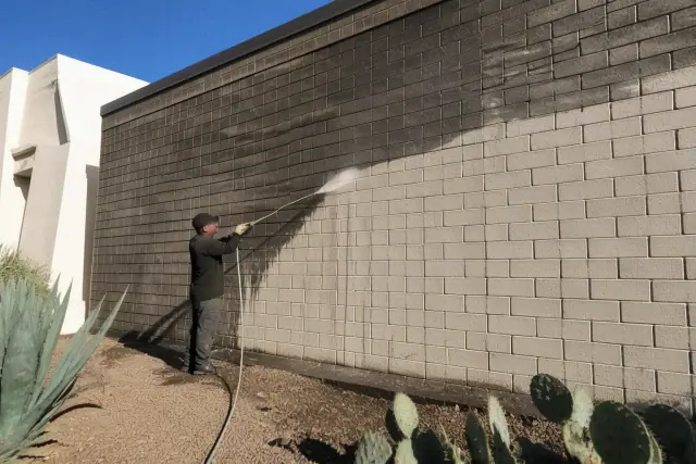 Pressure washing an industrial brick wall in Peoria, AZ, showing clean and dirty surfaces with water runoff.