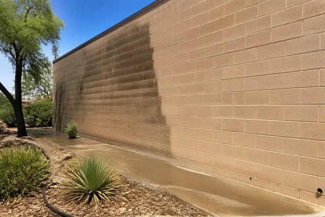 Commercial pressure washing of a brick building wall in Surprise, AZ, showing cleaned masonry and desert landscaping.