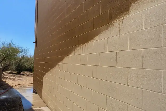 A contractor's photo of a commercial building wall showing a clean line between dirty and pressure-washed brick in Buckeye