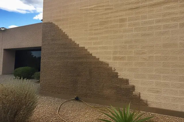A brick building wall showing a clear line between dirty and pressure-washed masonry in Chandler, AZ.
