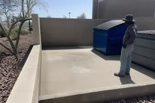 Cleaned concrete dumpster pad with grease removal and volcanic rock landscaping in Phoenix, AZ.