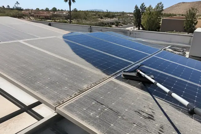 A technician cleaning commercial rooftop solar panels in Phoenix, AZ, showing a clear divide between dust and glass.