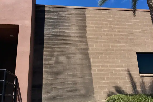 Pressure washing progress on a commercial building wall showing clean versus dirty brick in Phoenix, AZ.