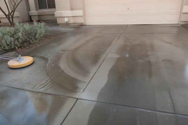 A pressure washer cleaning a residential concrete driveway with visible clean stripes in Surprise, AZ.