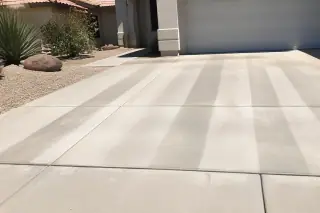 Cleaned concrete driveway with visible surface cleaner stripes and desert landscaping in Phoenix, AZ.