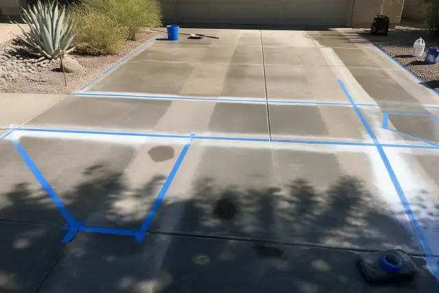 Worker preparing a concrete driveway for sealing with masking tape and templates in Phoenix, AZ.
