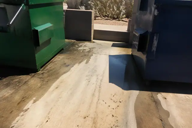 Pressure washing a commercial dumpster pad with grease removal in Scottsdale, AZ, surrounded by desert landscaping.