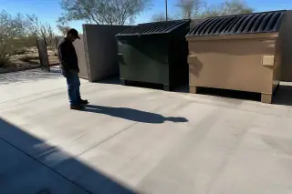 Technician inspecting a cleaned concrete dumpster pad surrounded by desert landscaping in Phoenix, AZ.