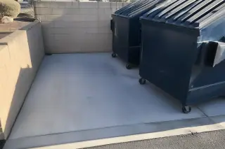 Cleaned concrete dumpster pad with grease and grime removed from near metal bins in Phoenix, AZ.
