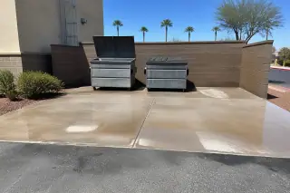 Cleaned concrete dumpster pad with grease removed from around metal trash bins and desert landscaping in Phoenix, AZ.