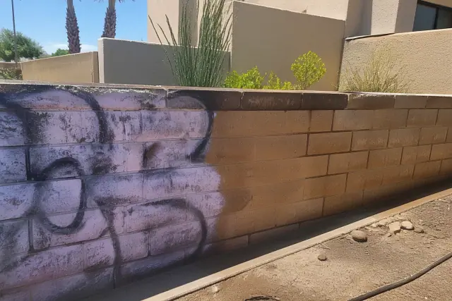 A partially cleaned brick wall showing graffiti removal in progress at a property in Phoenix, AZ.