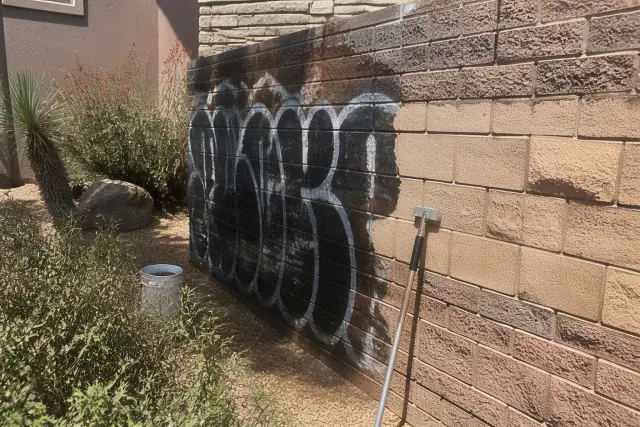 A brick wall in Phoenix, AZ, showing the removal of graffiti with wet spots and scraping tools on a desert property.