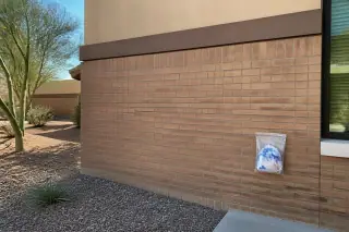Restored brick wall after graffiti removal with a sealed disposal pouch on gravel at a commercial site in Phoenix, AZ.