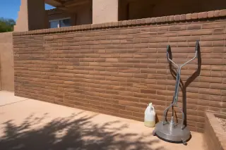 Restored brick masonry wall after graffiti removal with cleaning supplies on the ground in Phoenix, AZ.