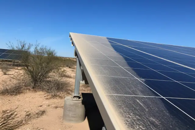 Technician cleaning dusty ground-mount solar panels in the desert sun in Phoenix, AZ.