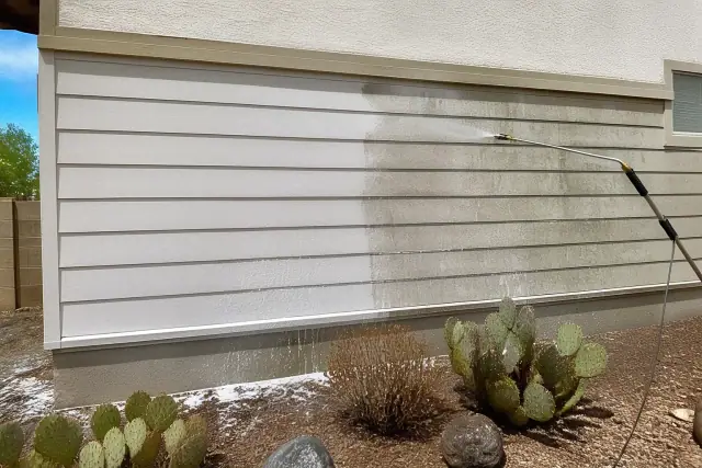Residential siding in Phoenix, AZ showing half-cleaned panels with suds and a rinsing wand near a prickly pear cactus.