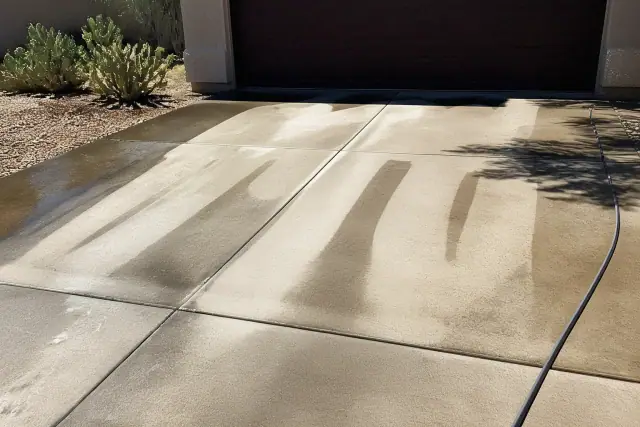A residential driveway in Phoenix, AZ, showing clean stripes from a surface cleaner next to dirty concrete and cacti.