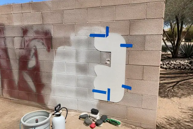 Contractor cleaning a paint spill off a brick wall in Phoenix, AZ, using removal tools and a masking template.