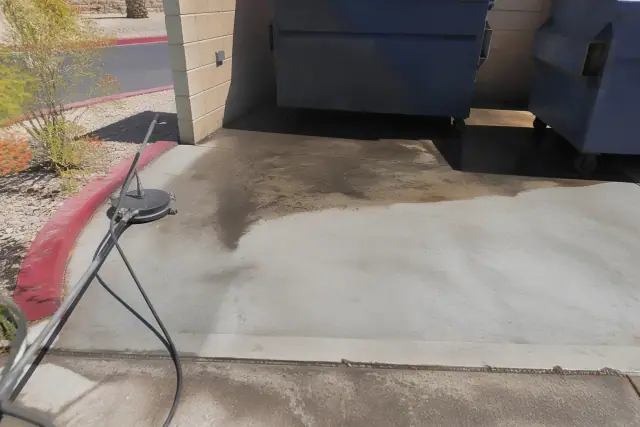 Cleaning a concrete dumpster pad with grime removal in a parking area in Glendale, AZ.