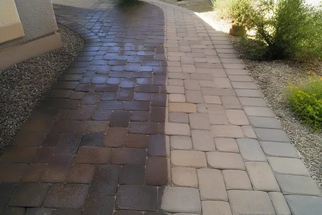 Stone paver walkway in Mesa, AZ showing the contrast between cleaned and untreated tiles near a stucco wall.