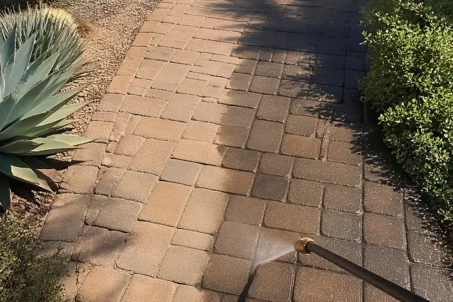 Technician cleaning and sealing an interlocking stone paver walkway in Peoria, AZ with desert succulents nearby.