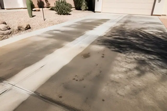 Concrete driveway in Phoenix, AZ, showing clean stripes from a surface cleaner next to oil stains and desert landscaping.