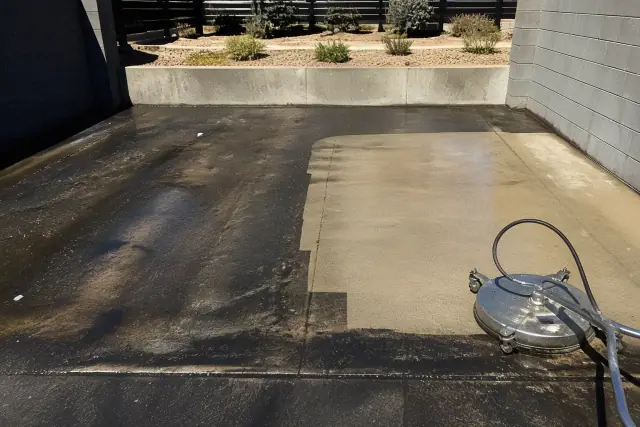 Concrete dumpster pad in Phoenix, AZ showing a clean patch amidst grease buildup with a pressure washer nozzle nearby.