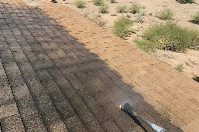 A pressure washer cleaning black algae off asphalt roof shingles in Buckeye, AZ.