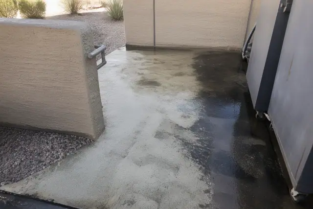 Concrete waste enclosure floor being pressure washed in Phoenix, AZ, showing clean concrete near metal trash bins.