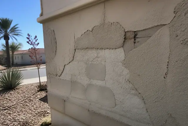 Cracked and crumbling stucco on a single-story house exterior in Phoenix, AZ with desert landscaping.