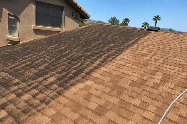 Sloped asphalt roof in Phoenix, AZ, showing the contrast between cleaned shingles and dark algae streaks.