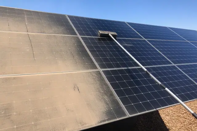 Technician cleaning dusty solar panels in Buckeye, AZ, showing a streak of clean reflective glass.