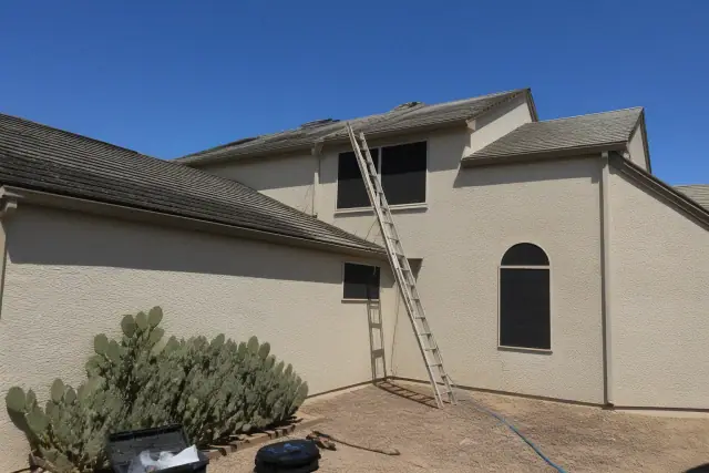 A contractor's photo of steep two-story roof access and cleaned asphalt shingles in Phoenix, AZ, with prickly pear cactus.