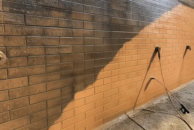 Technician cleaning dirty brick masonry on an industrial building wall in Phoenix, AZ.