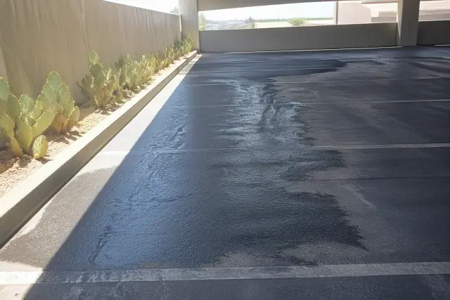 Spot treatment of oil stains on a Phoenix, AZ parking garage asphalt surface with nearby prickly pear cacti.