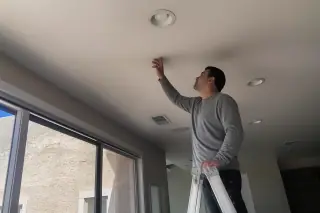Technician on a ladder inspecting a smooth ceiling drywall patch in a home in Phoenix, AZ.