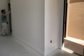 Technician checking a smooth drywall corner near an open doorway in a Phoenix, AZ home.