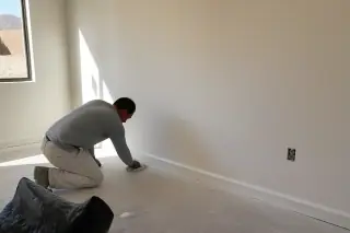 Technician cleaning dust from a smooth, sanded drywall seam transition in a Phoenix, AZ home.