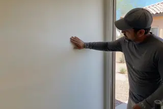 Technician inspecting a smooth drywall seam with desert landscaping visible through a window in a Phoenix, AZ home.