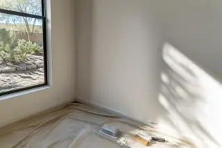 Drywall sanding block and brush on a drop cloth by a blended wall patch in a Phoenix, AZ home.