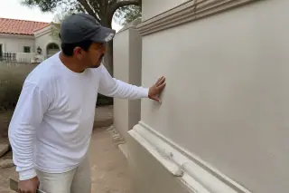 Professional checking a smooth plaster wall repair with desert landscaping visible in a Phoenix, AZ home.