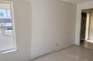 Damp plaster patch on an interior wall with sun-baked desert landscaping visible through the window in Phoenix, AZ.